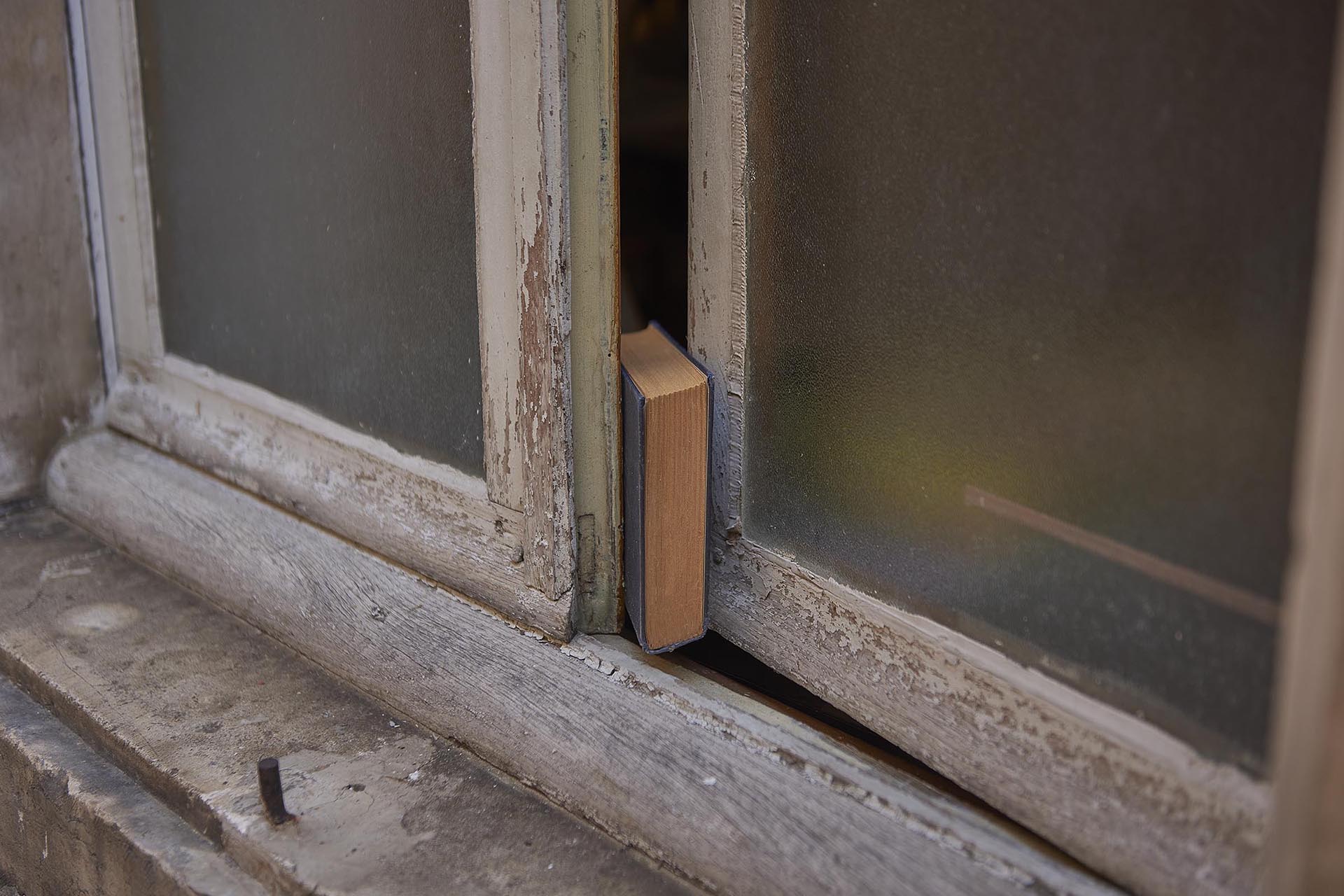 Random objects and places. A book keeps a window slightly ajar.